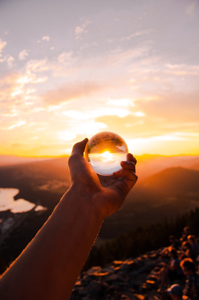 Home Captivating sunset view reflected in a crystal ball held by hand, overlooking a scenic landscape.
