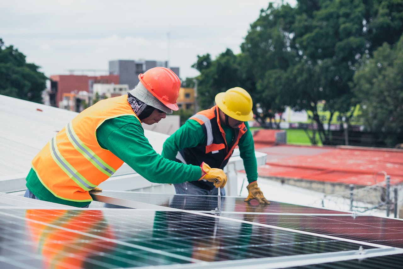 Home Two workers installing rooftop solar panels safely equipped with PPE and tools.
